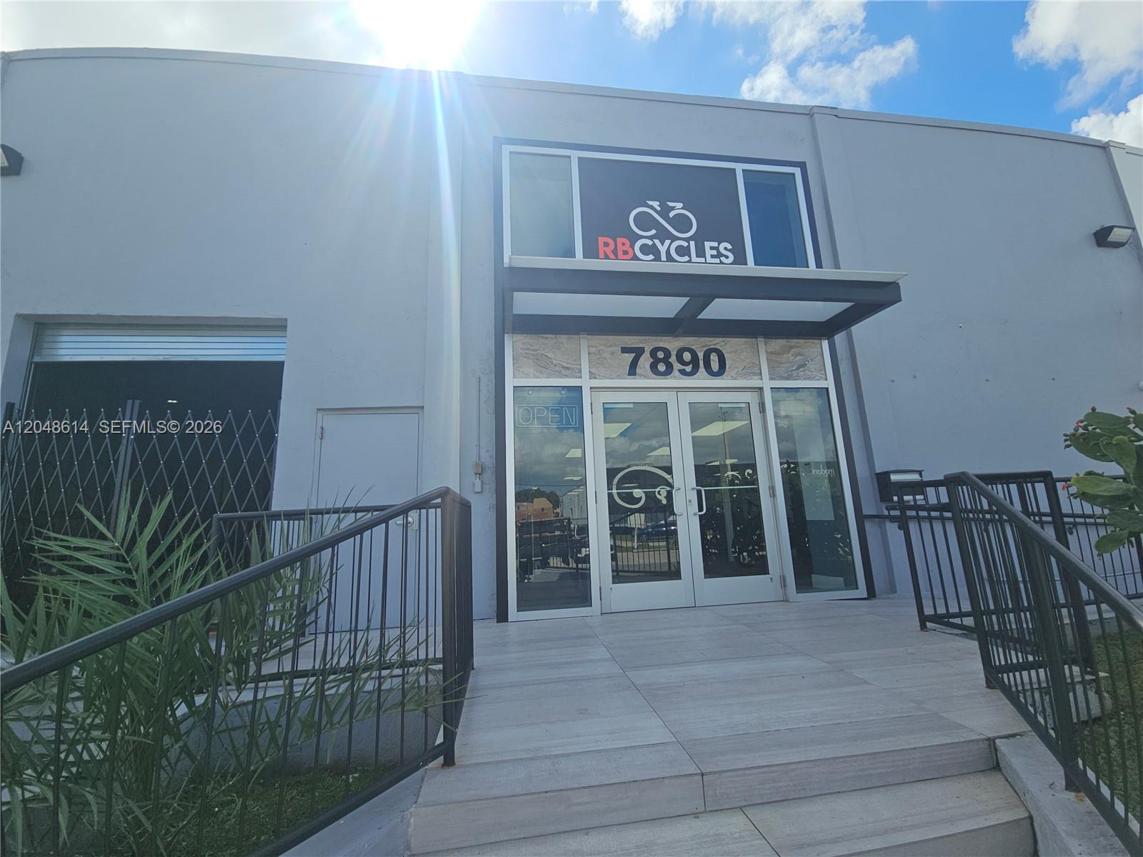 The exterior of a commercial building features a glass entrance with the sign RB CYCLES — 7890 NW 34th St, Doral FL 33122, DORAL, FL