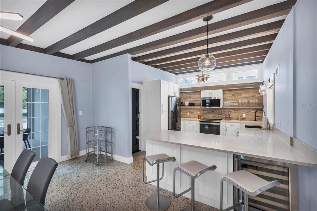A kitchen features white cabinetry, a quartz island with bar stools, and exposed ceiling beams — 1116 WESTWAY DRIVE, SARASOTA, FL