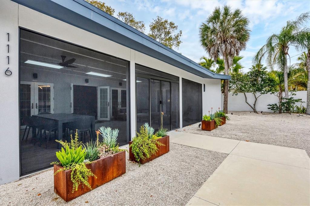 A modern home exterior features a screened-in patio, metal planters, and a gravel yard — 1116 WESTWAY DRIVE, SARASOTA, FL