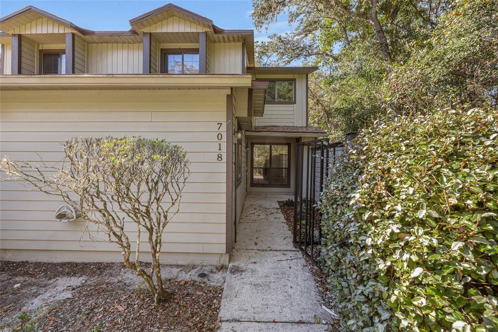 The exterior of a two-story tan house features a concrete walkway leading to the entrance — 7018 NW 52ND TERRACE, GAINESVILLE, FL