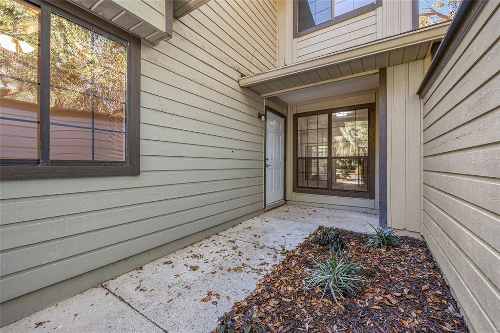 An exterior view of a home entrance with a concrete walkway and tan siding — 7018 NW 52ND TERRACE, GAINESVILLE, FL
