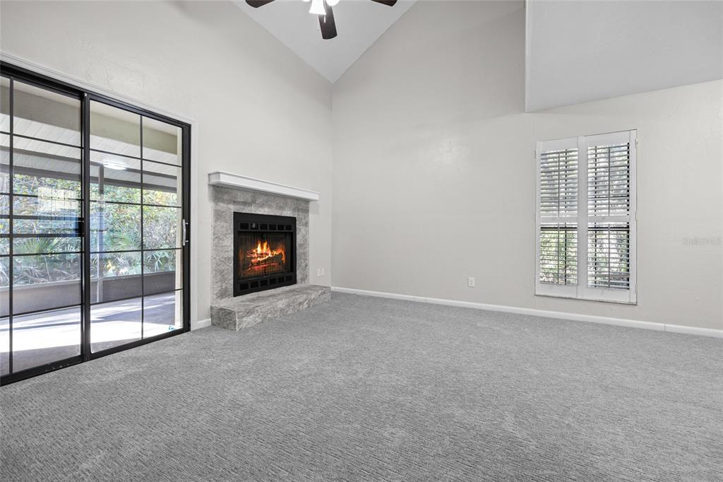 A living room with gray carpet, a stone fireplace, and sliding glass doors to a patio — 7018 NW 52ND TERRACE, GAINESVILLE, FL