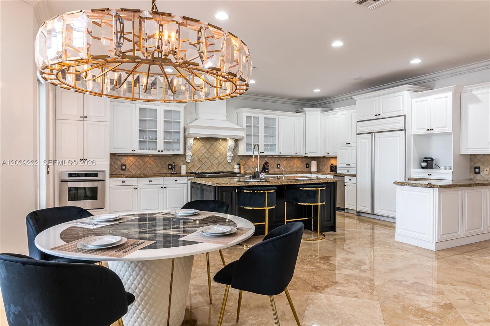 A kitchen and dining area features white cabinetry, a dark island, and a crystal chandelier — FORT LAUDERDALE, FL