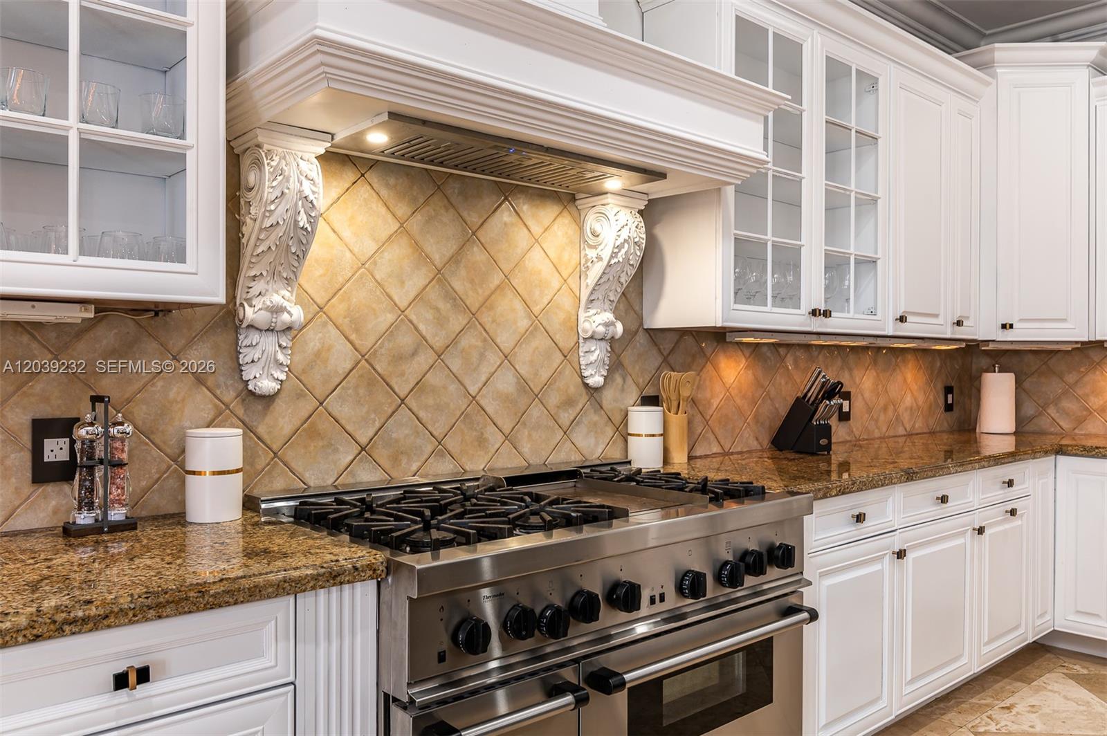 A kitchen features a stainless steel range, granite countertops, and white cabinets with glass doors — FORT LAUDERDALE, FL