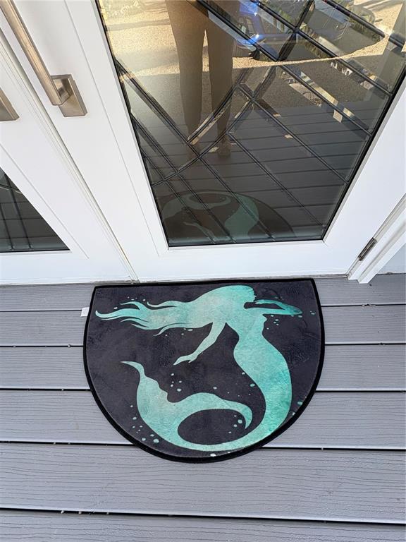 A semi-circular mermaid-themed doormat sits on a gray deck in front of a glass door — 5032 CALLE MINORGA, SARASOTA, FL