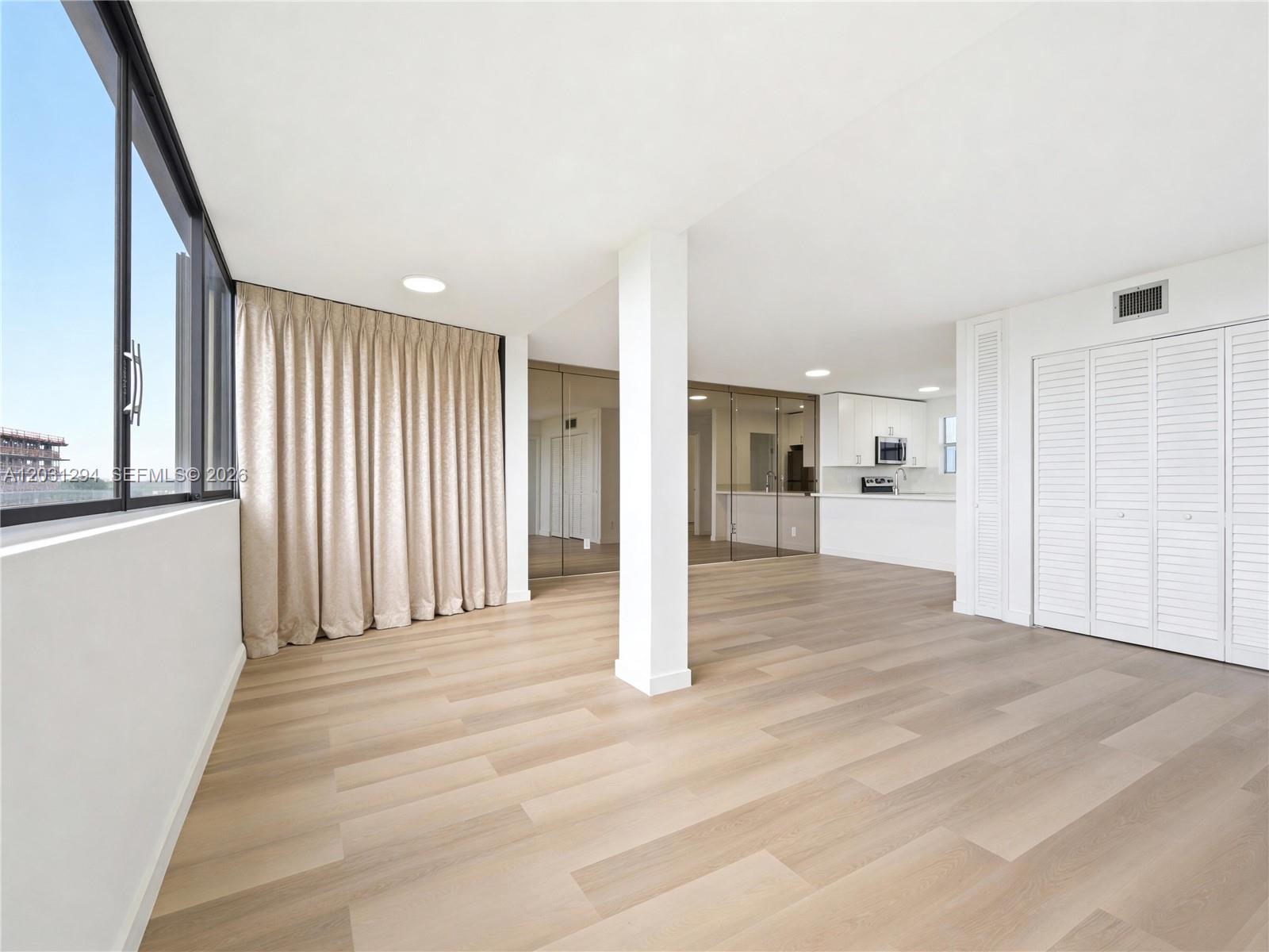 An open-concept living area features light wood flooring, a central support column, and a kitchen — 2950 SW 3rd Ave # 7F, Miami FL 33129, MIAMI, FL