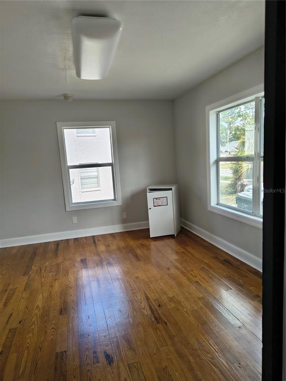 An empty room features hardwood floors, light gray walls, two windows, and a ceiling light — 1628 E GARY ROAD, LAKELAND, FL