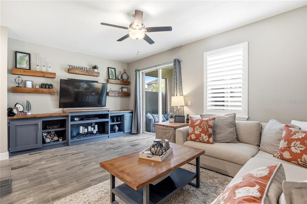 A living room features a grey media console, floating wood shelves, and a sectional sofa — 18892 ULMUS STREET, LUTZ, FL