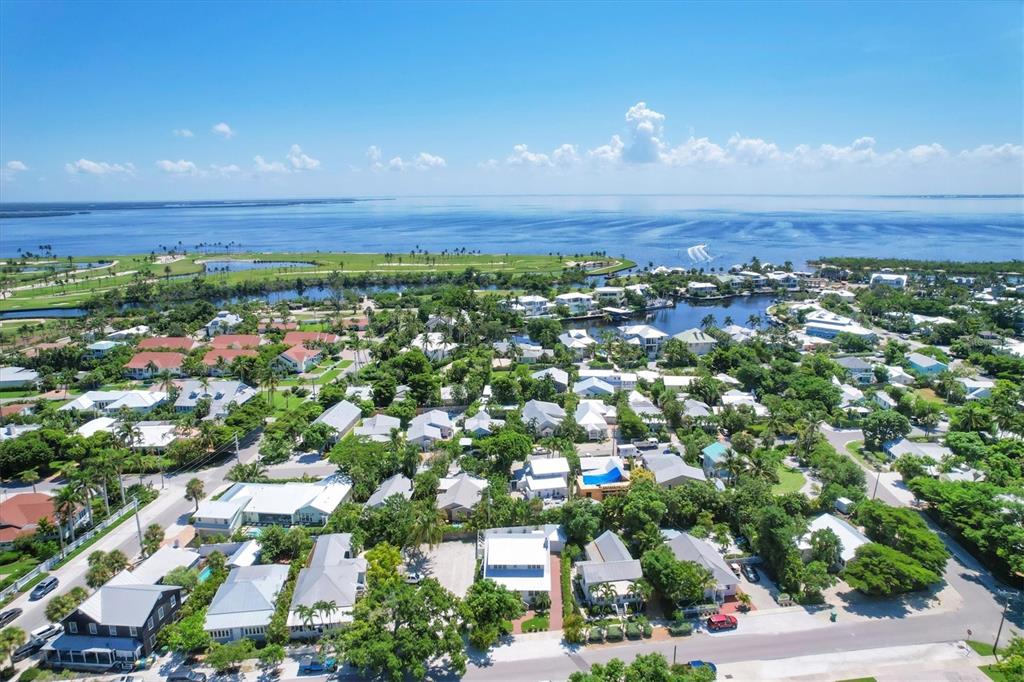 An aerial view shows a coastal neighborhood with houses, lush trees, and a nearby bay — 342 PALM AVENUE, BOCA GRANDE, FL