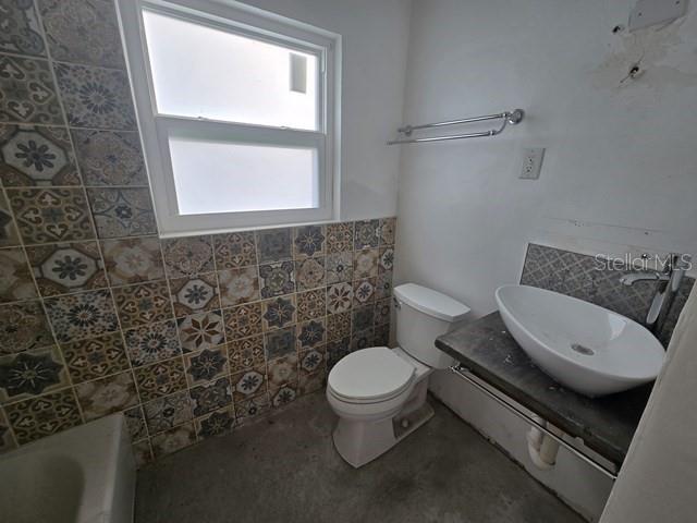 A bathroom features patterned wall tiles, a white toilet, and a vessel sink on a counter — 3615 HIGEL AVENUE, SARASOTA, FL