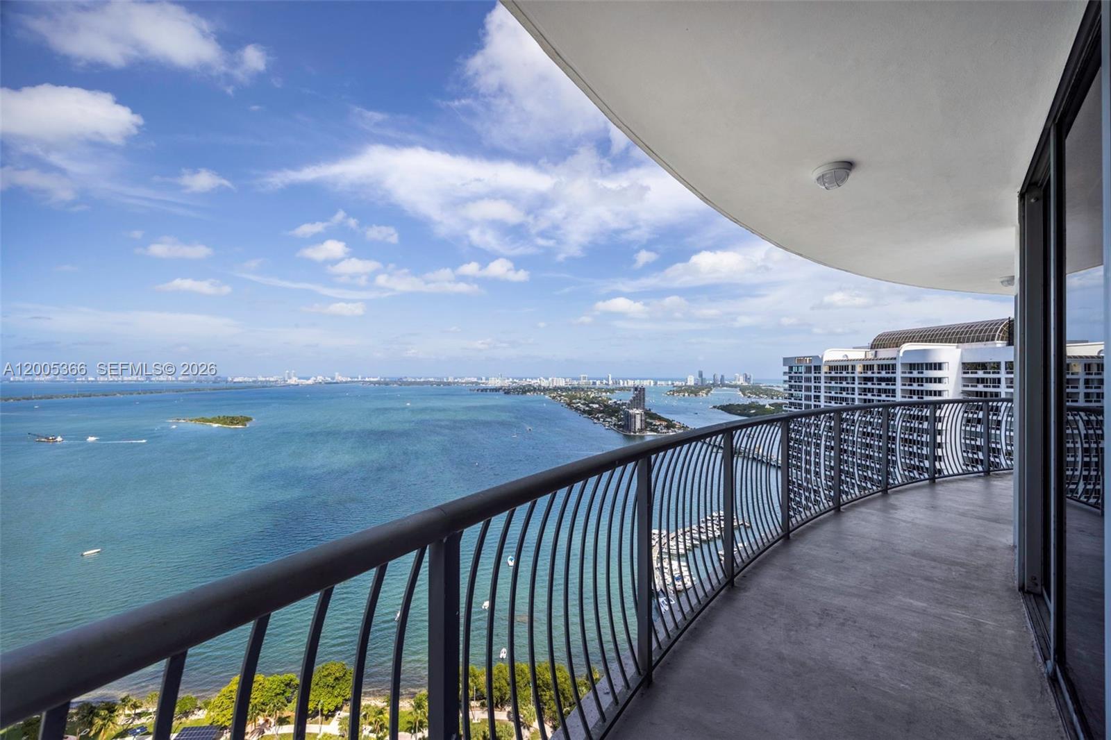 A high-rise balcony overlooks a large bay with a distant city skyline under a blue sky — 1750 N Bayshore Dr # 3801, Miami FL 33132, MIAMI, FL