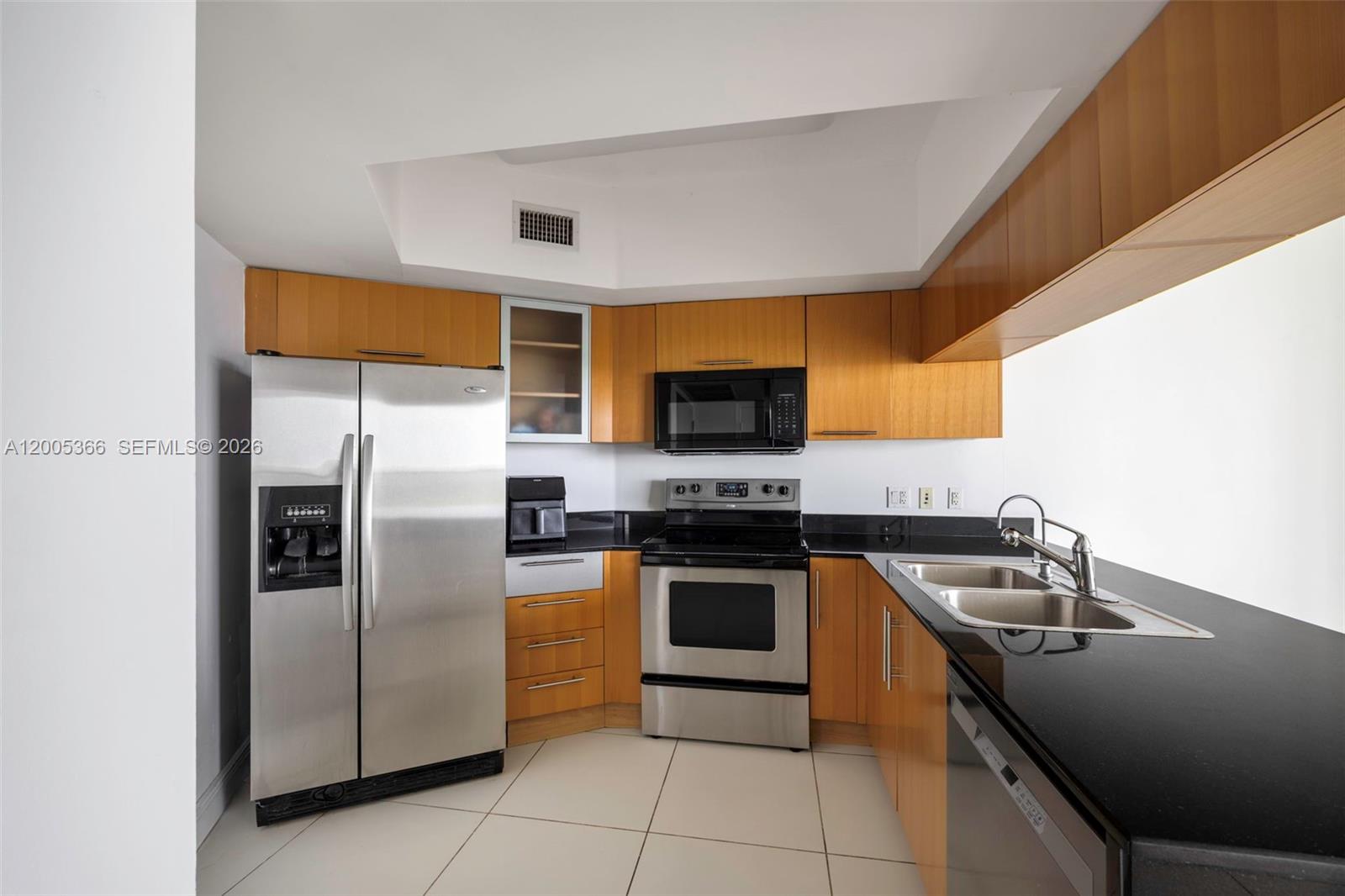 A kitchen features stainless steel appliances, wood cabinets, and black countertops on a tiled floor — 1750 N Bayshore Dr # 3801, Miami FL 33132, MIAMI, FL