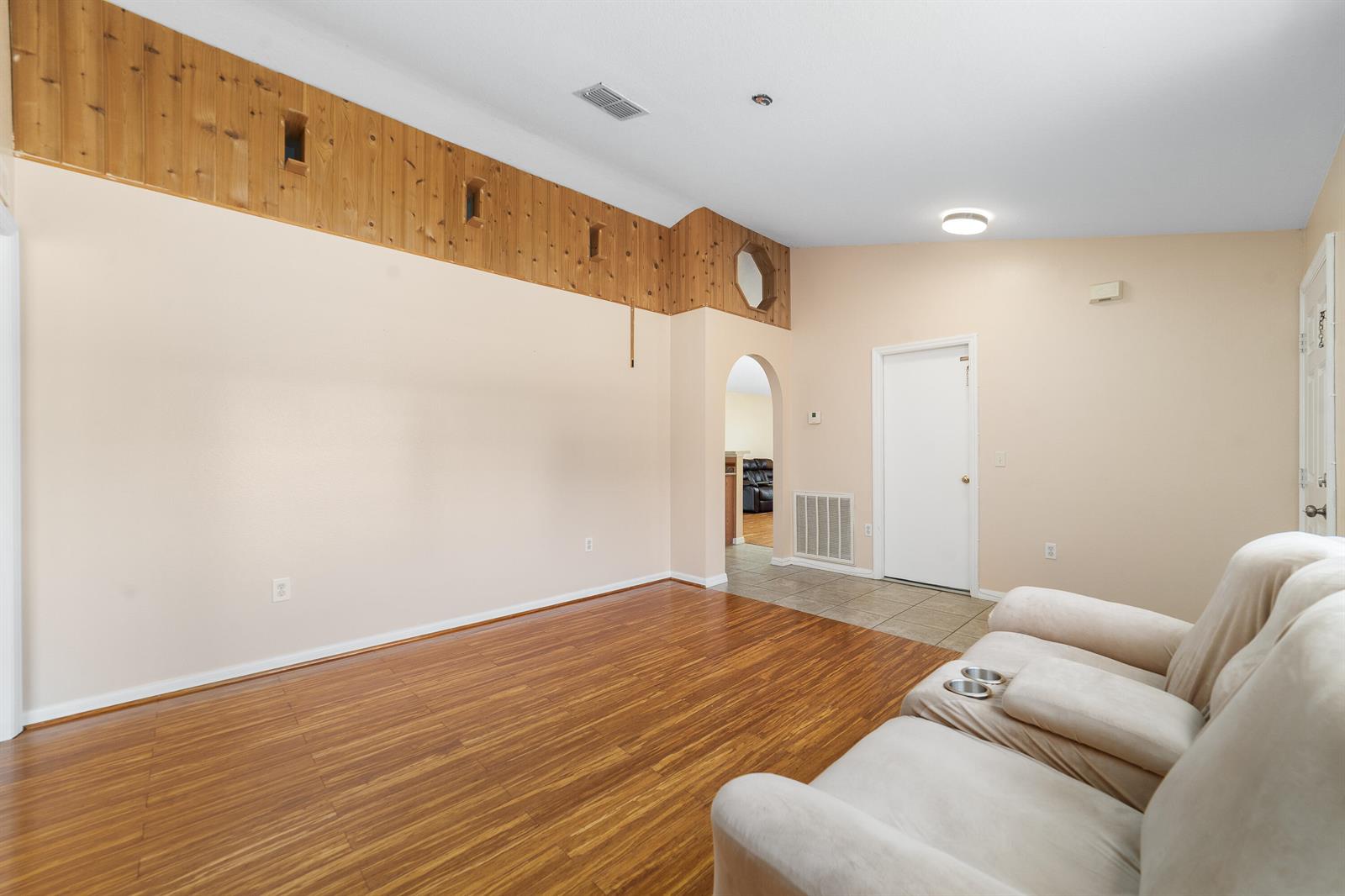 A living room features wood-paneled upper walls, light-colored paint, wood flooring, and a beige sofa — 1165 SE 40th Avenue, Okeechobee FL 34974, OKEECHOBEE, FL