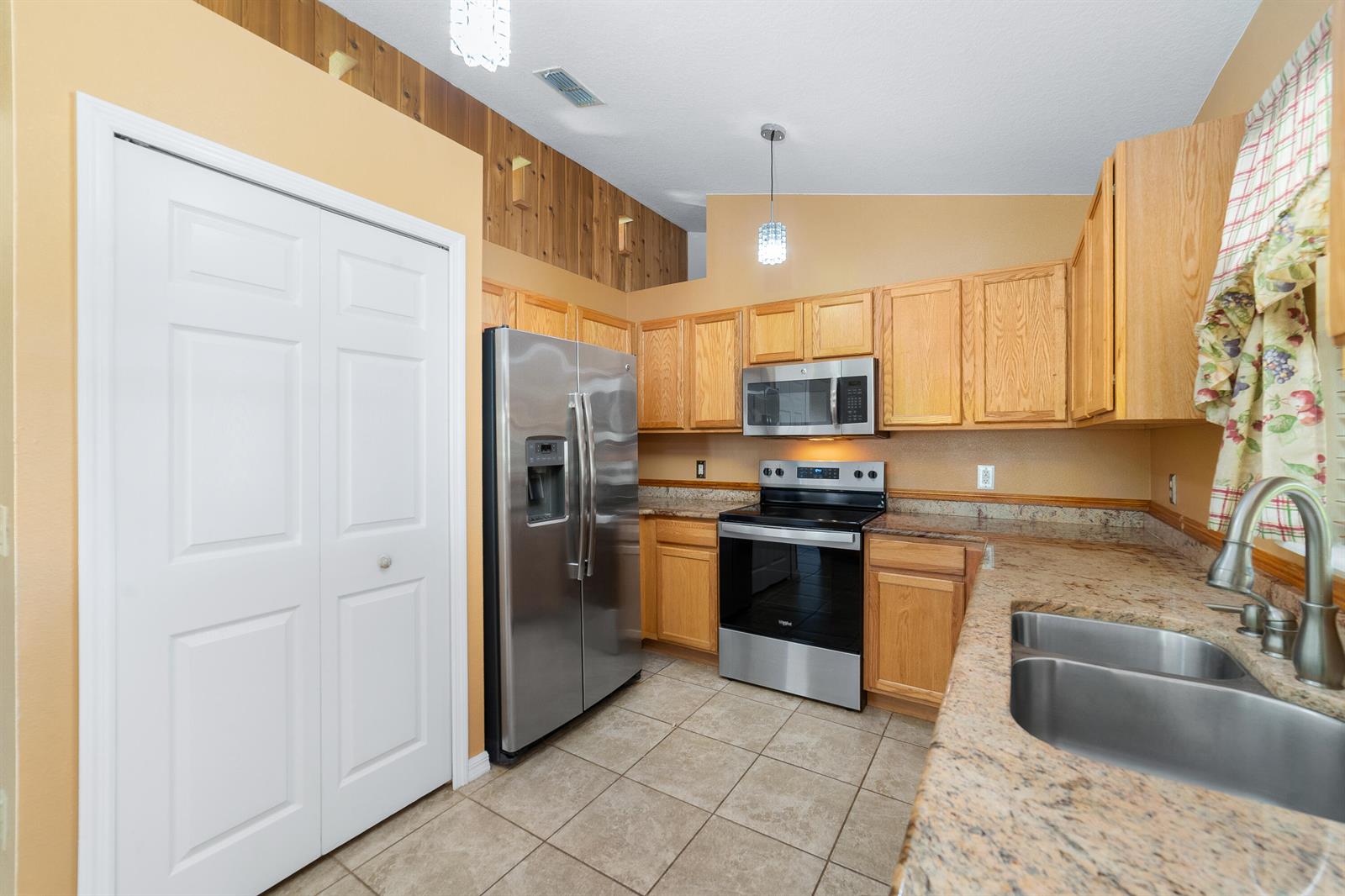 A kitchen features light wood cabinets, granite countertops, stainless steel appliances, and wood-paneled accent walls — 1165 SE 40th Avenue, Okeechobee FL 34974, OKEECHOBEE, FL