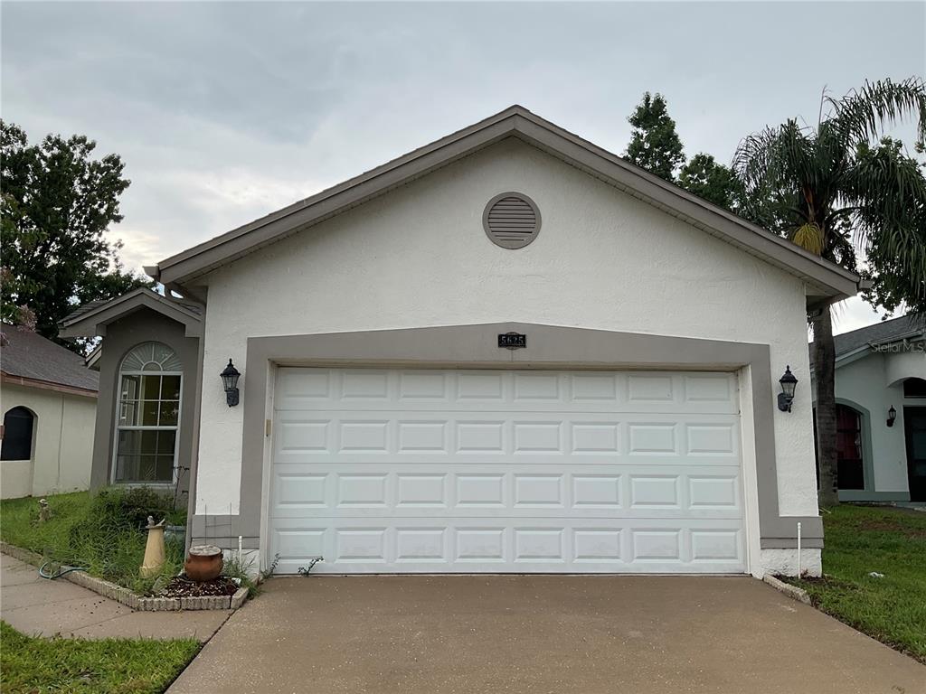 A single-story house exterior features a white stucco facade, a two-car garage, and a driveway — 5625 ARNOLD ZLOTOFF DRIVE, ORLANDO, FL