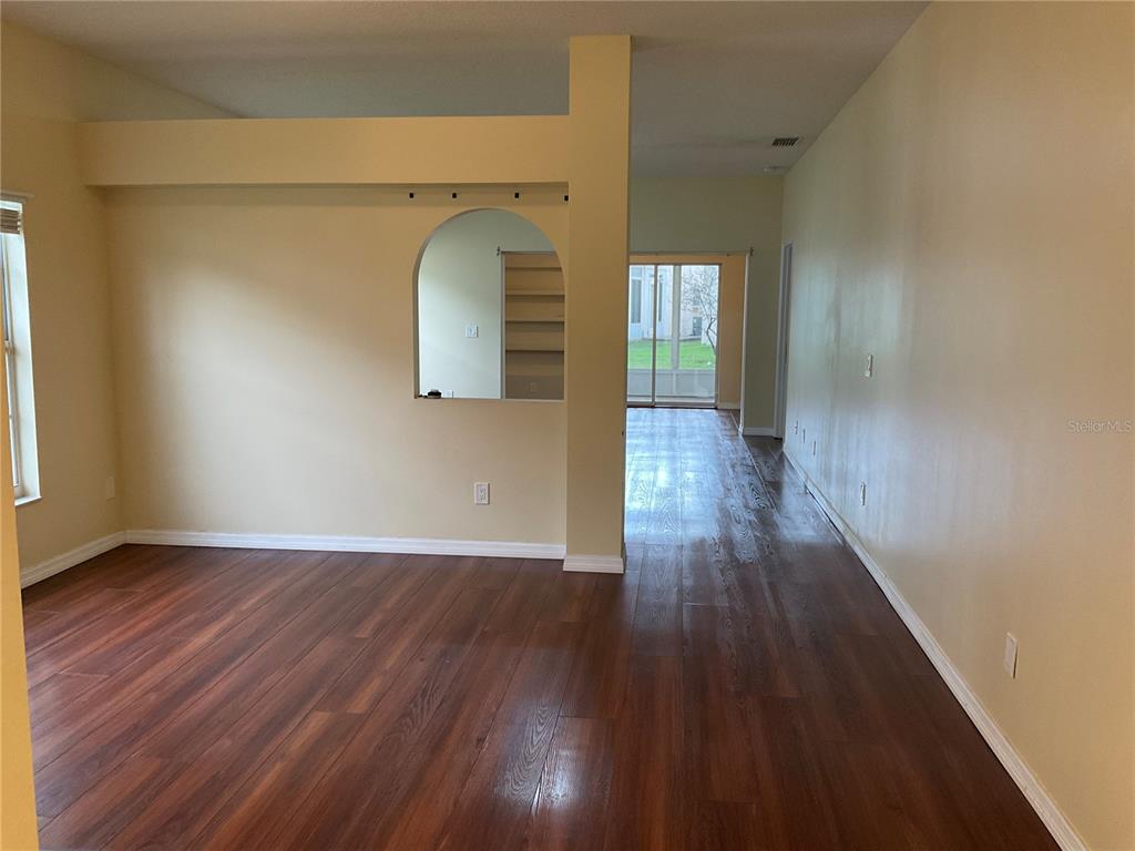 An empty living room features dark wood flooring, beige walls, and an arched wall cutout — 5625 ARNOLD ZLOTOFF DRIVE, ORLANDO, FL