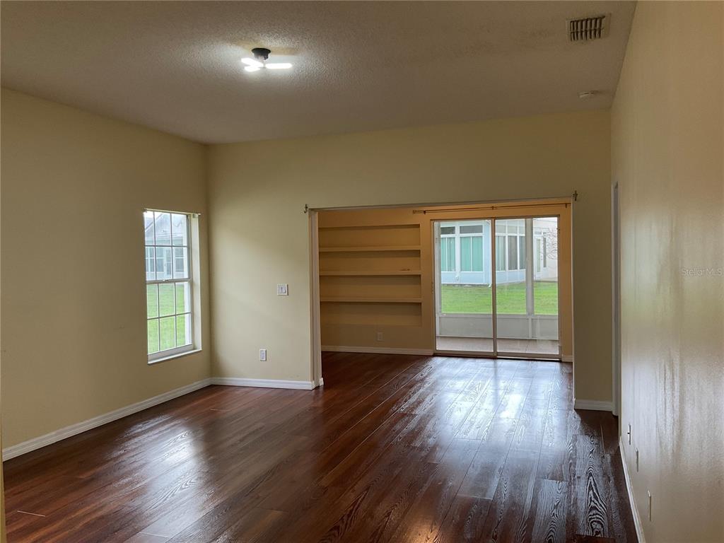 A living room with dark wood flooring, a built-in bookshelf, and a sliding glass door — 5625 ARNOLD ZLOTOFF DRIVE, ORLANDO, FL