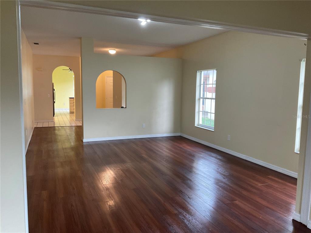 An empty living room features dark wood-look flooring, beige walls, and an arched wall cutout — 5625 ARNOLD ZLOTOFF DRIVE, ORLANDO, FL