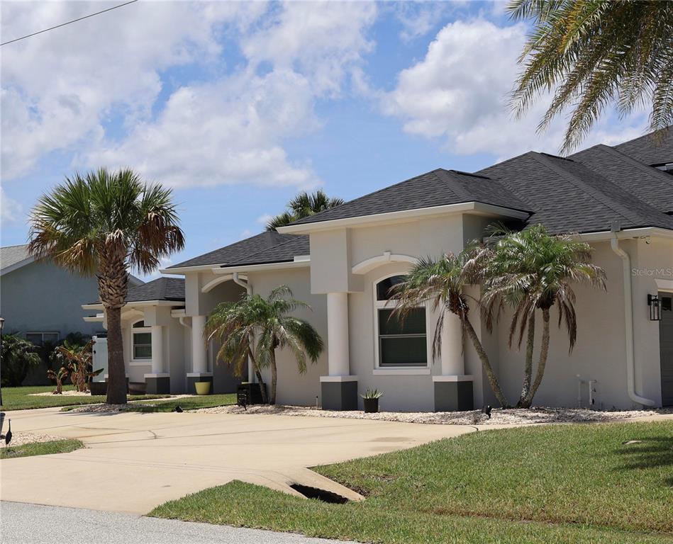 A single-story house with a beige stucco exterior, dark roof, and palm trees in front — 2 COLONY COURT, PALM COAST, FL