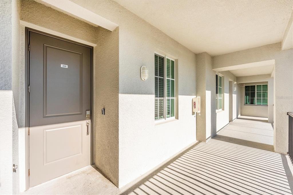 An exterior view of an apartment building hallway with a numbered door and windows — 12280 WELLEN GOLF STREET UNIT 205, VENICE, FL
