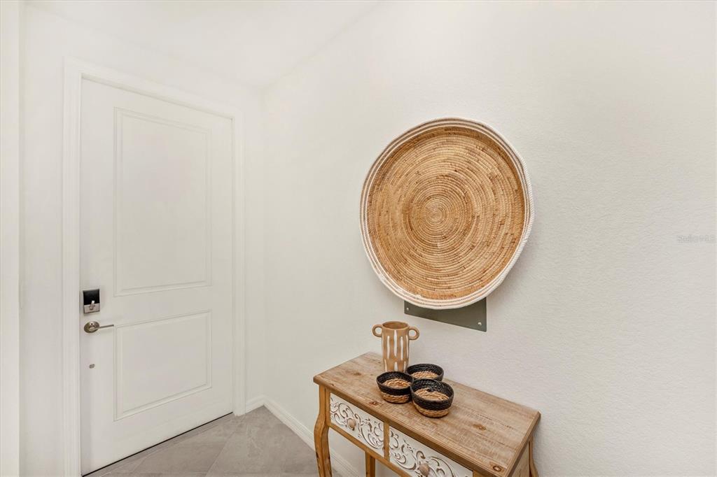 A white door stands next to a wooden console table topped with decorative bowls — 12280 WELLEN GOLF STREET UNIT 205, VENICE, FL