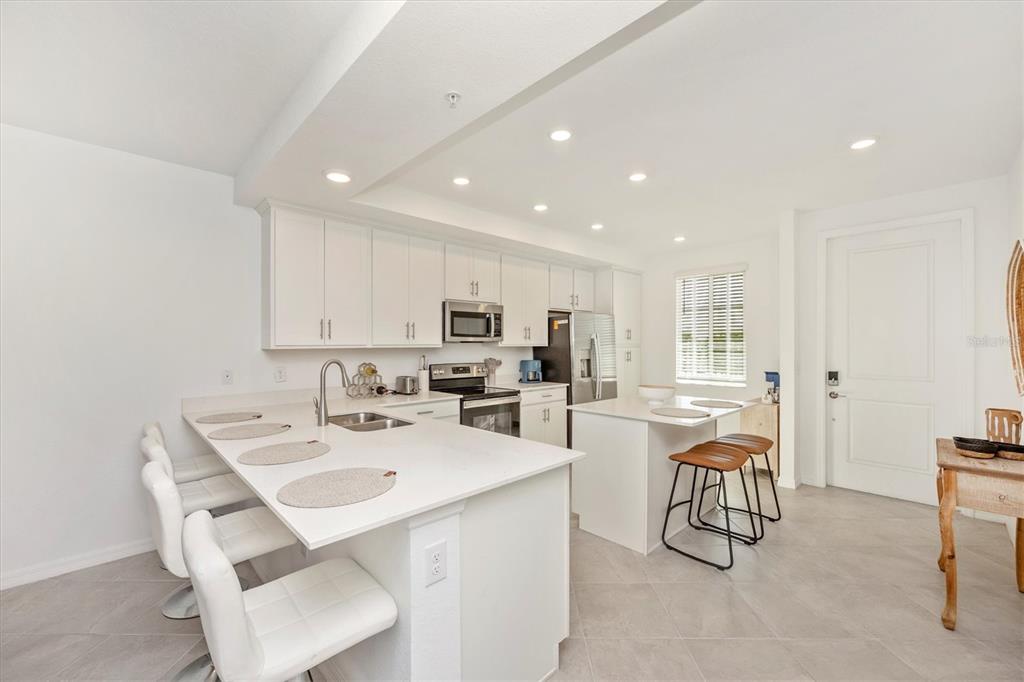 A modern kitchen features white cabinetry, quartz countertops, a breakfast bar, and stainless steel appliances — 12280 WELLEN GOLF STREET UNIT 205, VENICE, FL