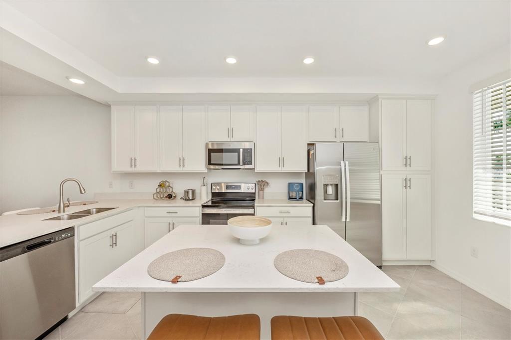 A modern kitchen features white cabinetry, stainless steel appliances, and a central island with seating — 12280 WELLEN GOLF STREET UNIT 205, VENICE, FL