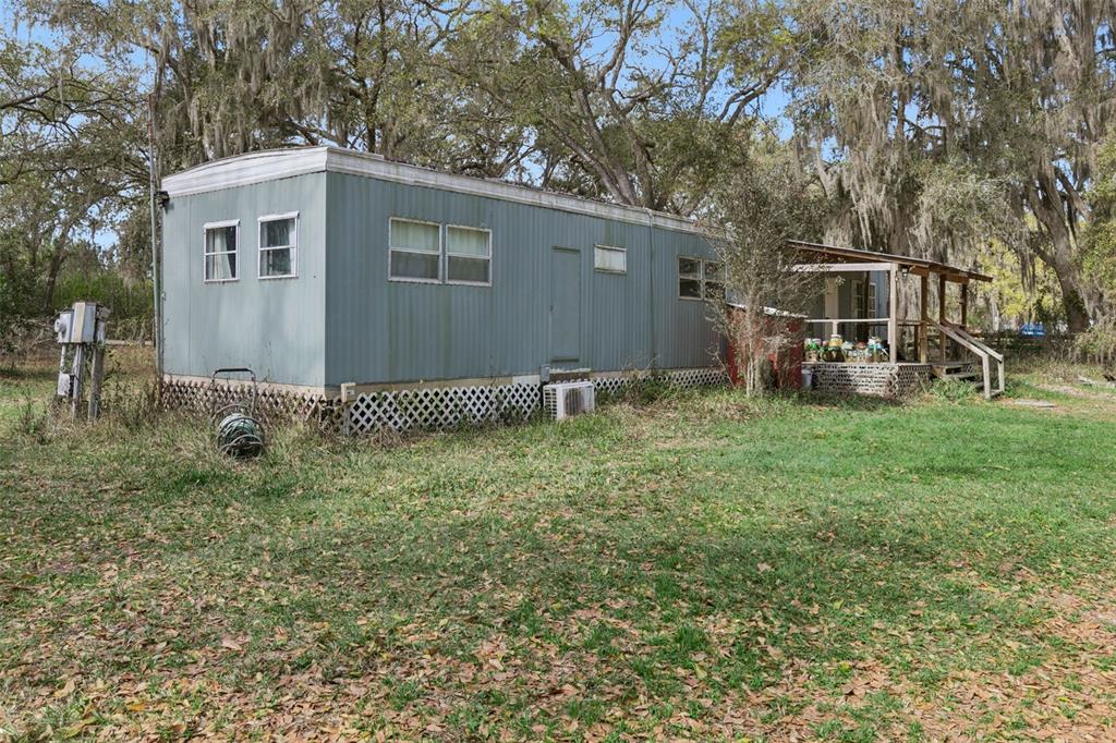 A single-wide mobile home with a covered porch sits on a grassy lot with trees — 15527 TROUSDALE STREET, CLERMONT, FL