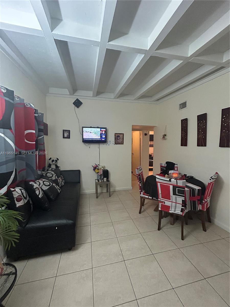 A living and dining area features a black sofa, a small dining set, and exposed ceiling beams — 1080 NW 121st St, North Miami FL 33168, NORTH MIAMI, FL