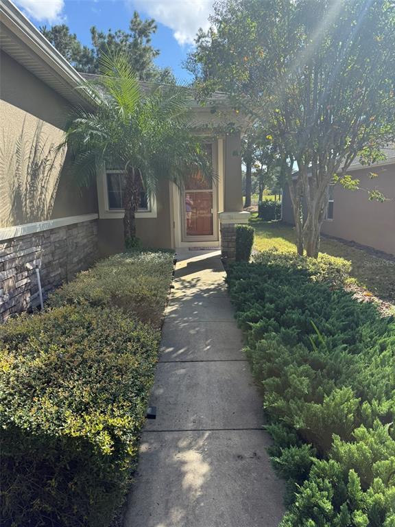 A concrete walkway leads to the front entrance of a house with stone siding — 21846 BELGIAN COURT, MOUNT DORA, FL