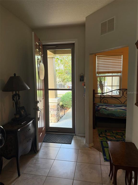 An entryway with tile flooring leads to an open doorway revealing a bedroom — 21846 BELGIAN COURT, MOUNT DORA, FL