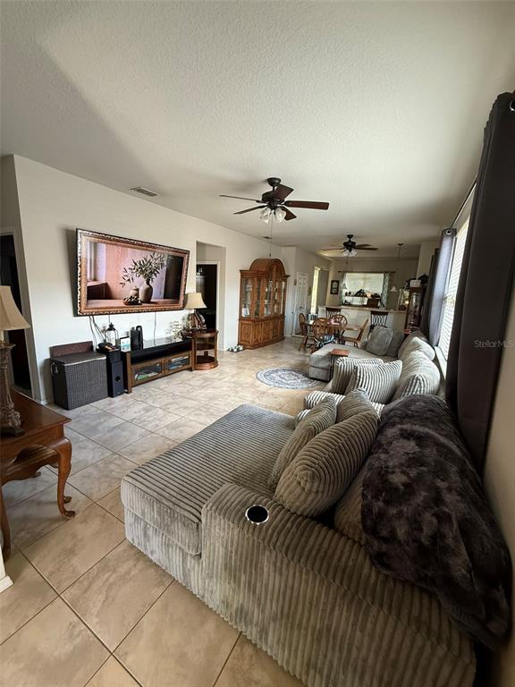 A living room features a large sectional sofa, tile flooring, and a wall-mounted television — 21846 BELGIAN COURT, MOUNT DORA, FL