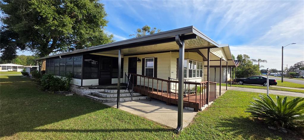 A single-story mobile home features a screened-in porch, a wooden ramp, and a metal carport — 5650 BENTON STREET, ZEPHYRHILLS, FL