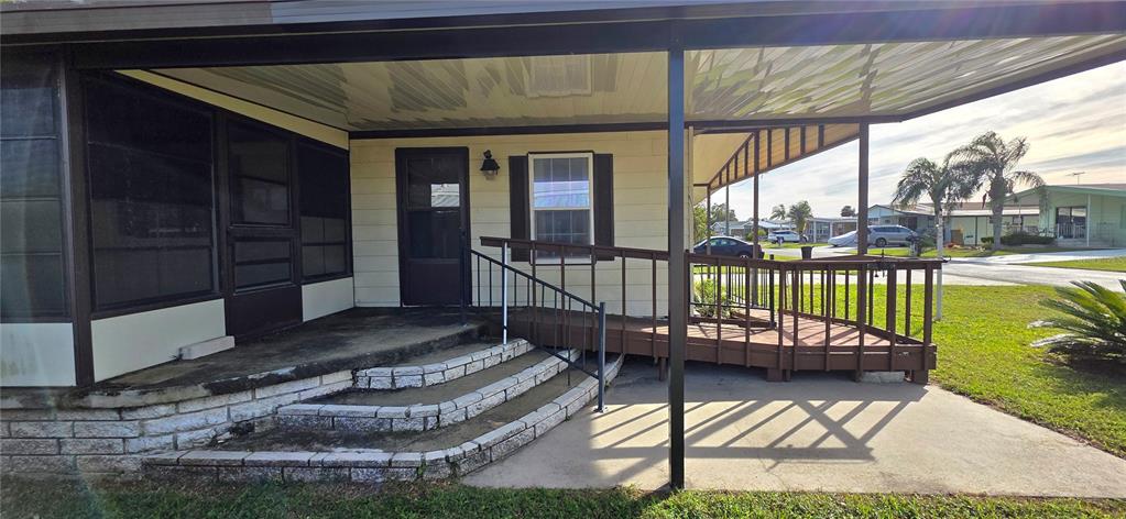 A mobile home exterior features a covered patio, concrete steps, and a wooden wheelchair ramp — 5650 BENTON STREET, ZEPHYRHILLS, FL