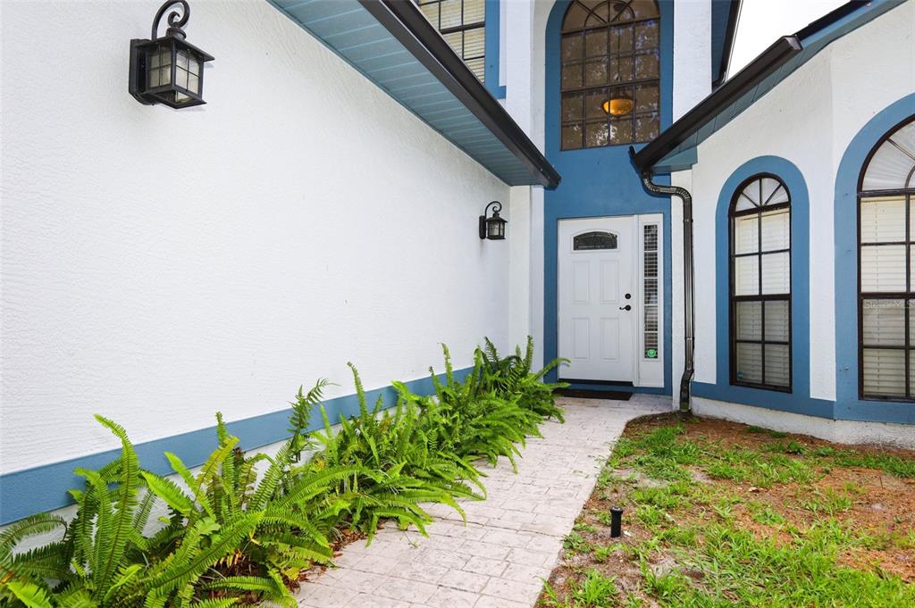 A white house exterior features blue trim, a paved walkway, and a row of ferns — 1152 TWIN RIVERS BOULEVARD, OVIEDO, FL