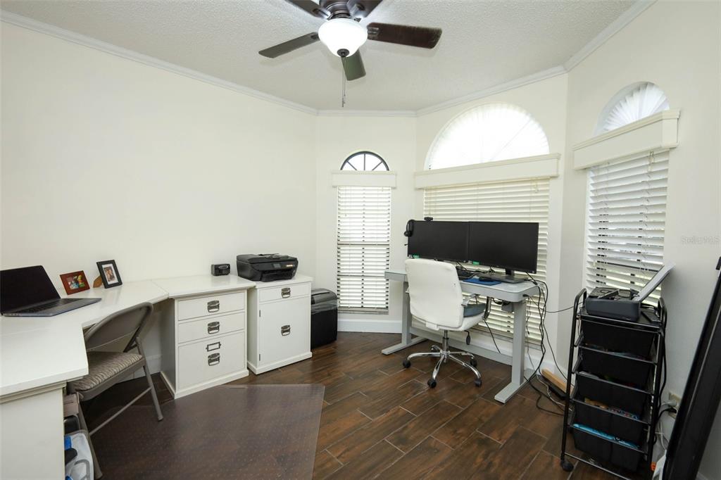 A home office features a dual-monitor desk, a separate workspace, and dark wood-look tile flooring — 1152 TWIN RIVERS BOULEVARD, OVIEDO, FL