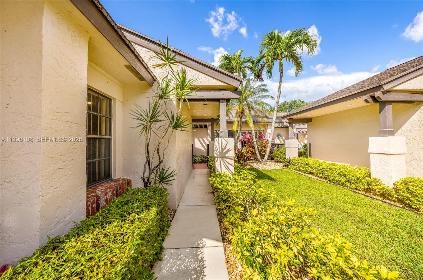 A concrete walkway leads toward a covered entryway between two sections of a stucco house — 5302 Fairway Woods Dr # 4612, Delray Beach FL 33484, DELRAY BEACH, FL