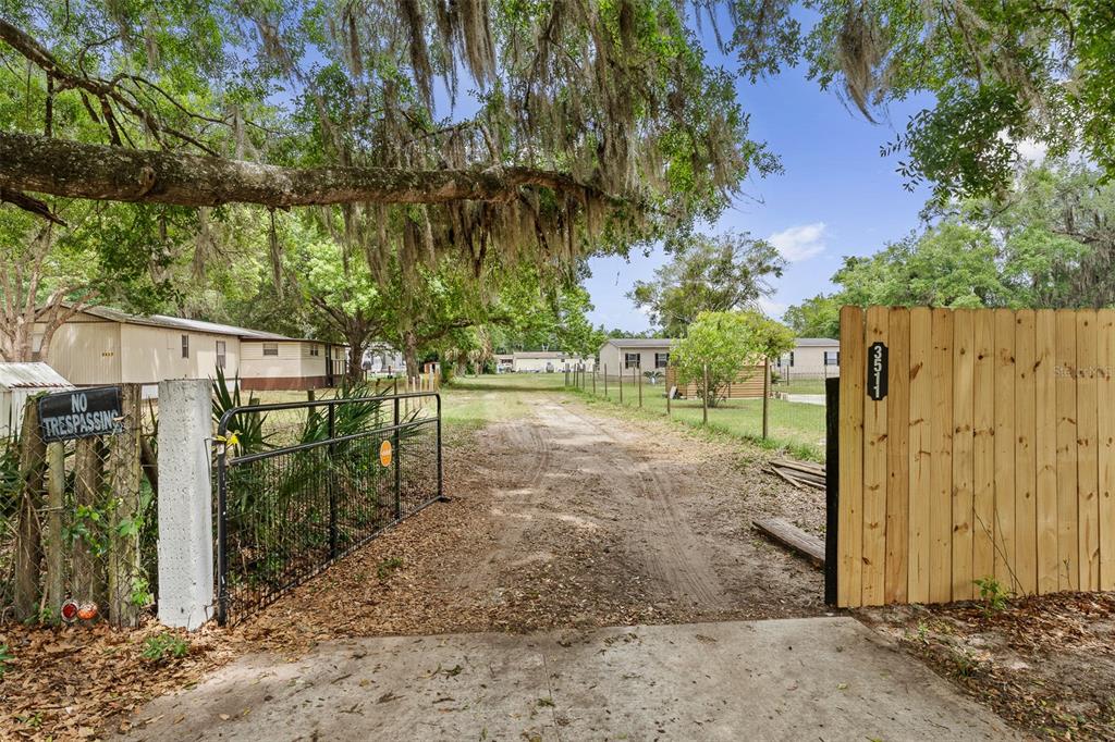 A dirt driveway leads through an open metal gate between a wooden fence and trees — 3511 S PALM AVENUE, PALATKA, FL