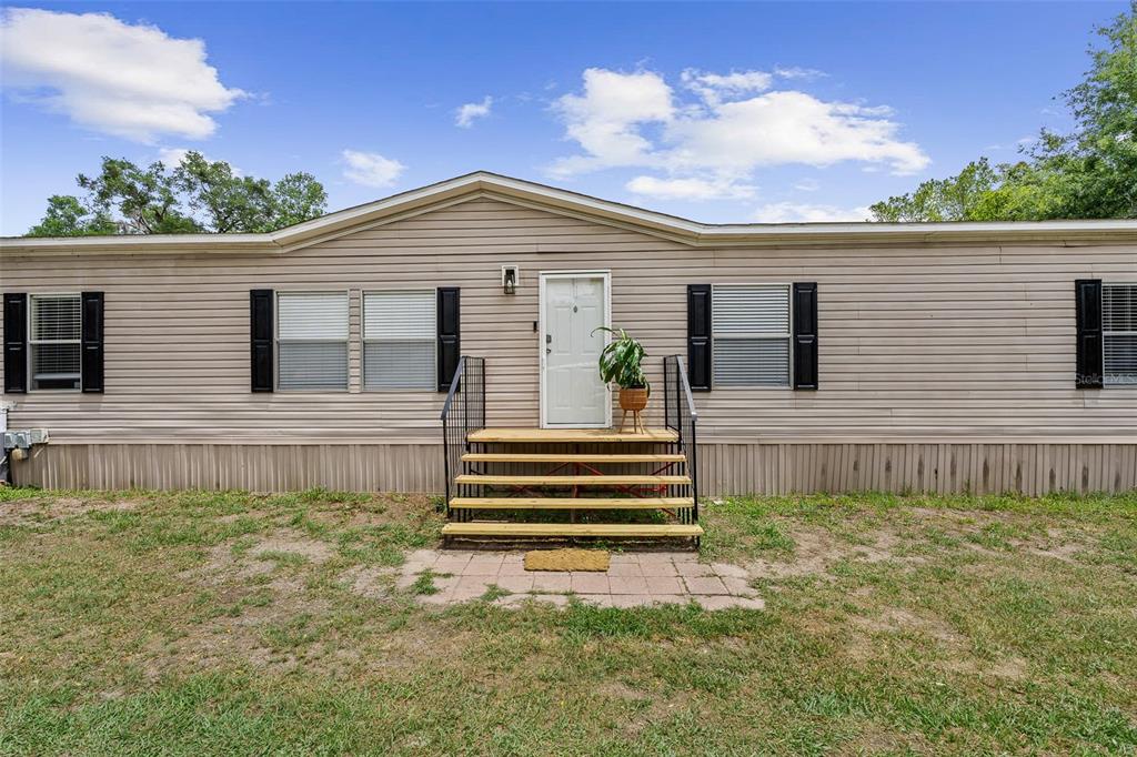 A single-story manufactured home with tan siding, black shutters, and a wooden front staircase — 3511 S PALM AVENUE, PALATKA, FL