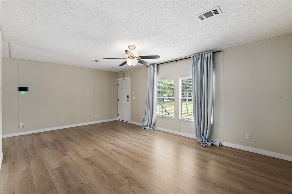 An empty living room features light wood-look flooring, beige walls, and a ceiling fan — 3511 S PALM AVENUE, PALATKA, FL