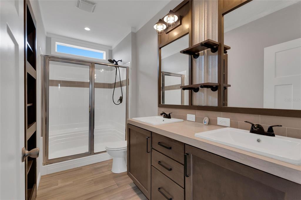A bathroom features a double vanity, a glass-enclosed shower, and wood-look flooring — 25294 CANTERBURY DRIVE, LAKE WALES, FL