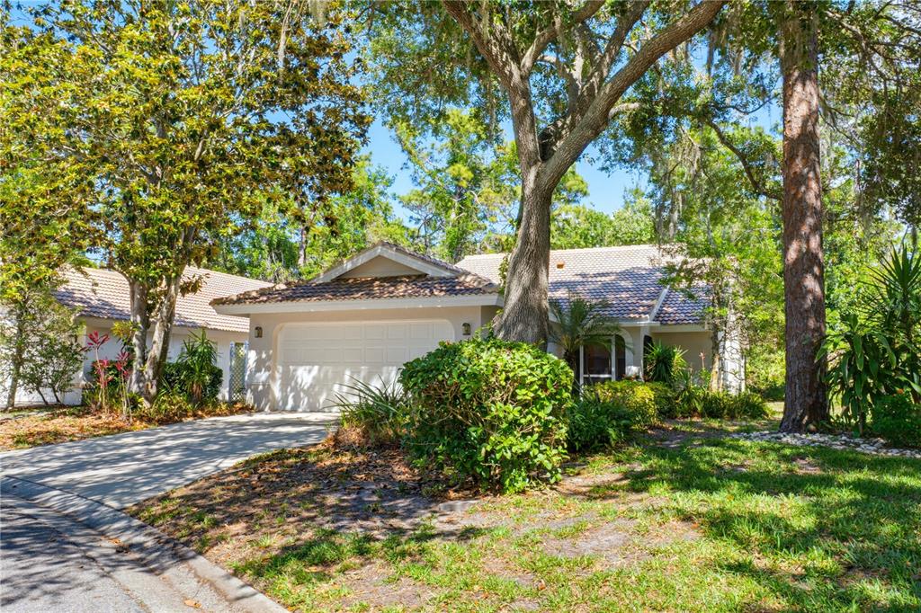 A single-story house with a white garage, tiled roof, and mature trees in the yard — 4779 TIVOLI PLACE, SARASOTA, FL