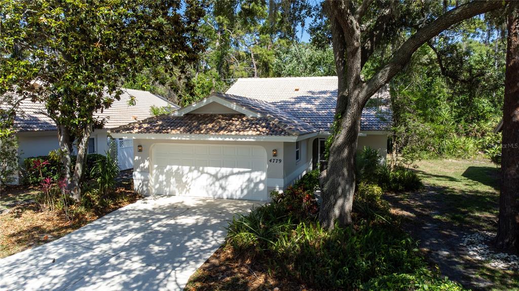 A single-story house with a white garage door, tiled roof, and surrounding trees — 4779 TIVOLI PLACE, SARASOTA, FL