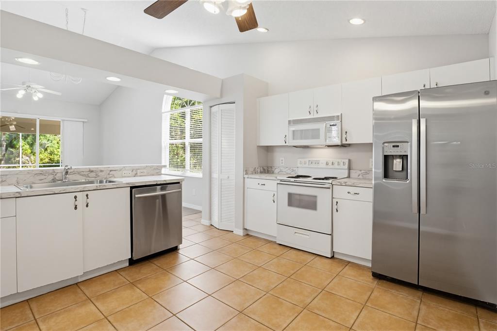 A kitchen features white cabinets, stainless steel appliances, marble-look countertops, and tan tile flooring — 4779 TIVOLI PLACE, SARASOTA, FL