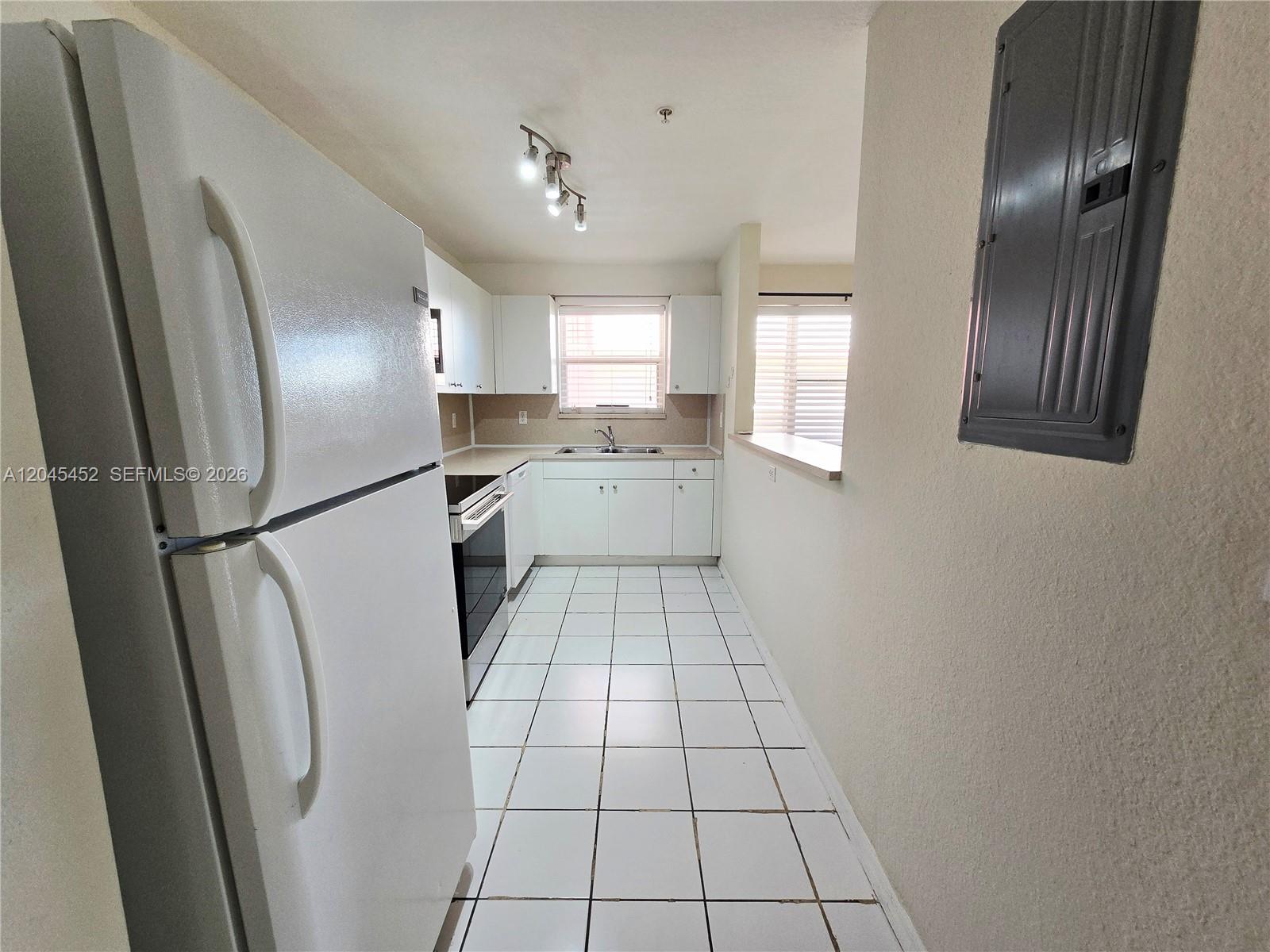 A galley-style kitchen features white cabinets, a white refrigerator, and white tiled flooring — 1627 NW 18th St # 201, Miami FL 33125, MIAMI, FL