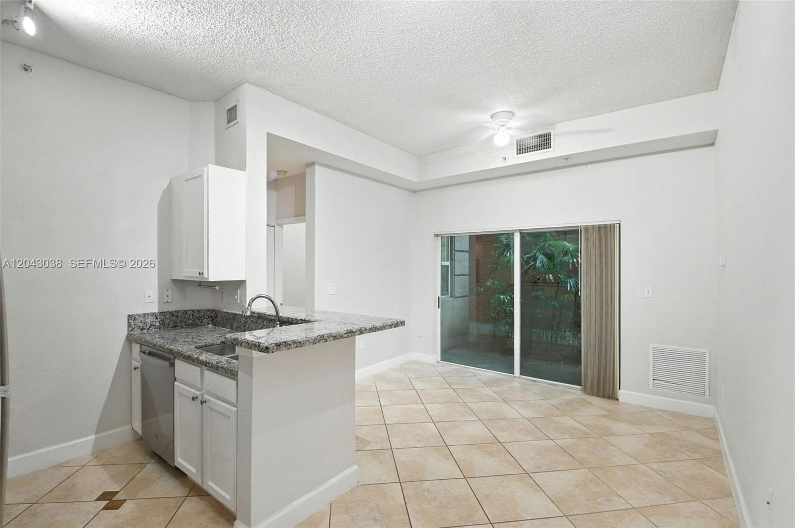 A kitchen with granite countertops and white cabinets opens to a tiled living area — 6001 SW 70th St # 108, South Miami FL 33143, SOUTH MIAMI, FL