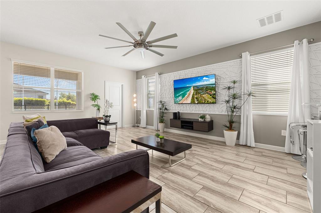 A living room features a large gray sectional, a wall-mounted television, and wood-look tile flooring — 9044 SAND TRAP DRIVE, DAVENPORT, FL