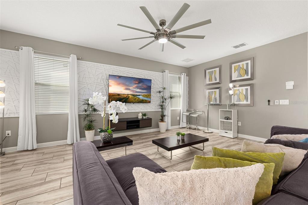 A living room features a wall-mounted television, a ceiling fan, and a gray sectional sofa — 9044 SAND TRAP DRIVE, DAVENPORT, FL