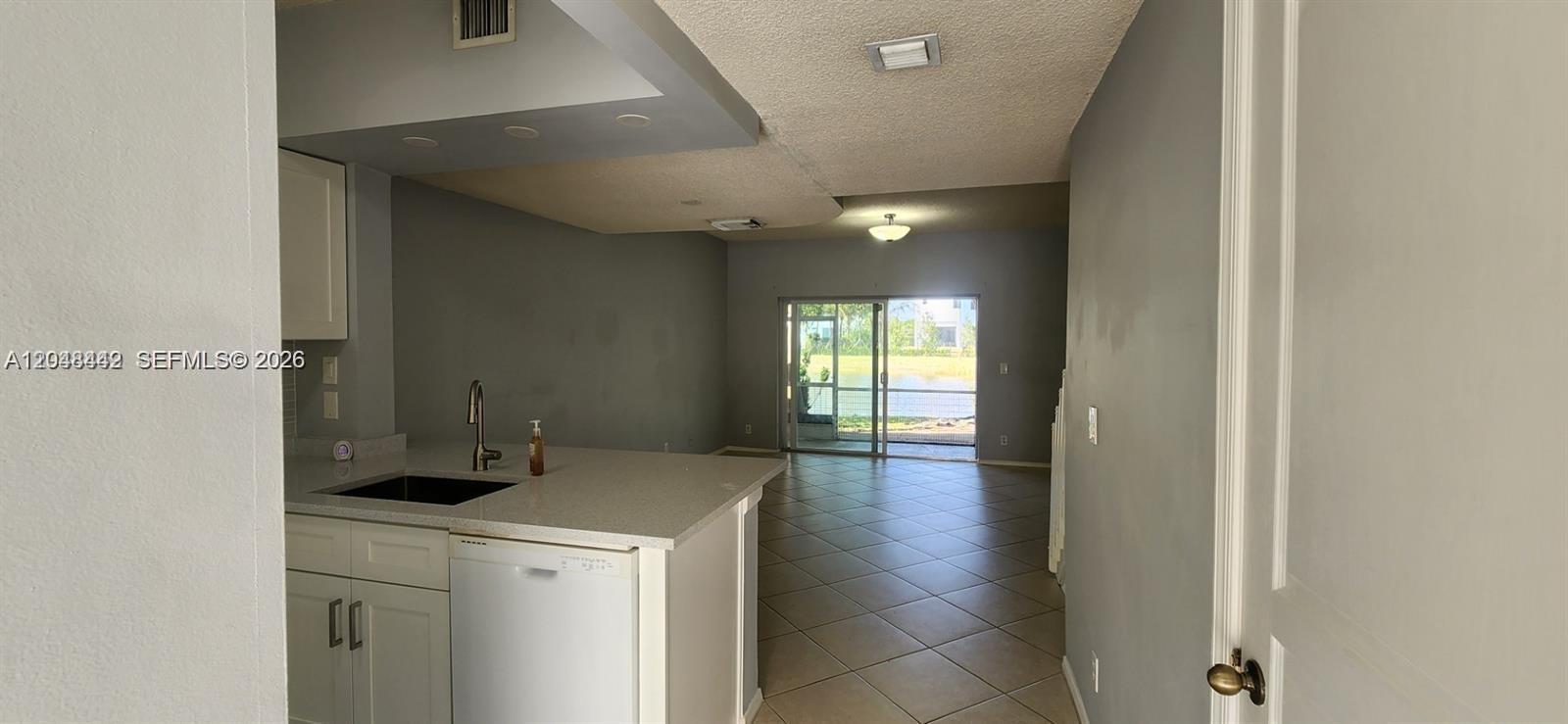 A kitchen with white cabinets and a breakfast bar opens into a tiled living area — 211 Mallory Ct, Weston FL 33326, WESTON, FL