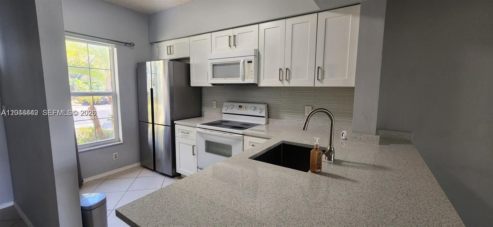 A kitchen features white cabinets, stainless steel appliances, a speckled countertop, and a window — 211 Mallory Ct, Weston FL 33326, WESTON, FL